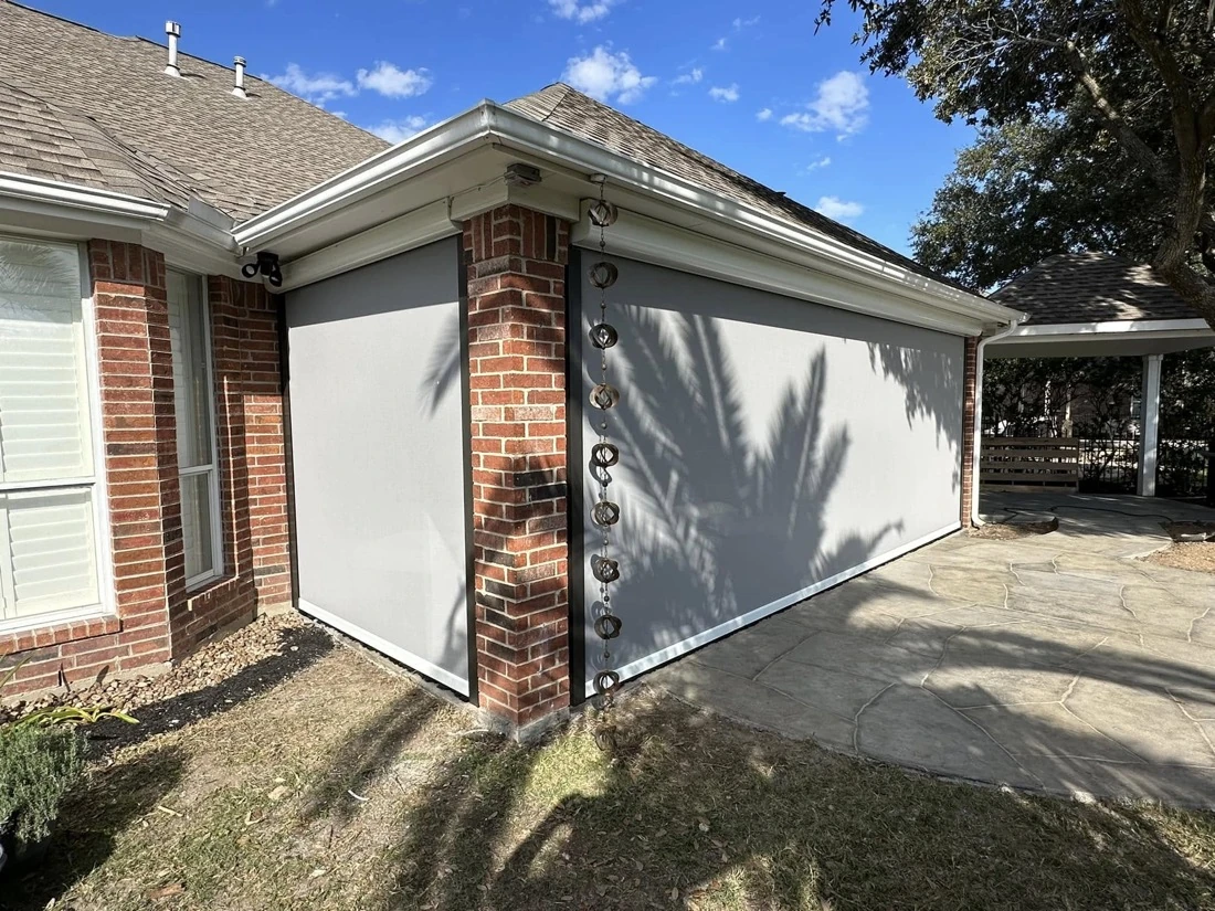 Motorized drop shades lowered over the openings of a brick covered patio